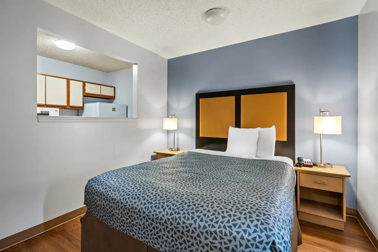 Extended-stay guest room with queen bed, television, work area and kitchenette