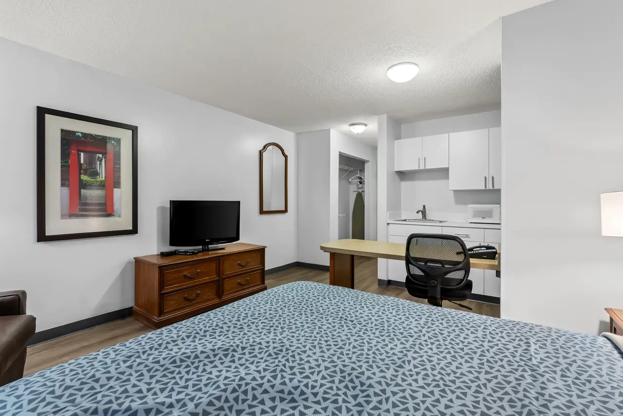 Spacious guest room with queen bed, television, desk and kitchenette